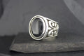Elegant silver ring with a polished black stone and intricate side designs.