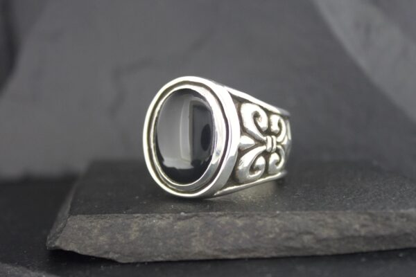 Elegant silver ring with a polished black stone and intricate side designs.