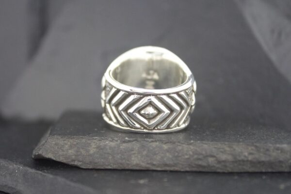 Silver ring with geometric diamond patterns on a dark surface.