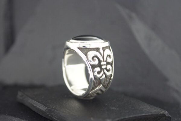 Silver ring with intricate black floral patterns on a dark surface.