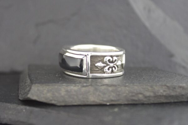 A silver ring with a fleur-de-lis design on a stone surface.