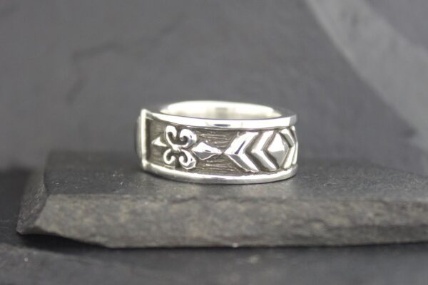 Silver ring with arrow and fleur-de-lis design on textured band.