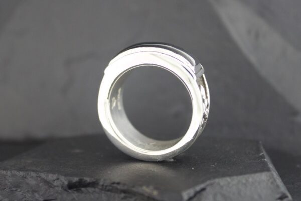 Close-up of a silver ring with a textured design on a dark surface.