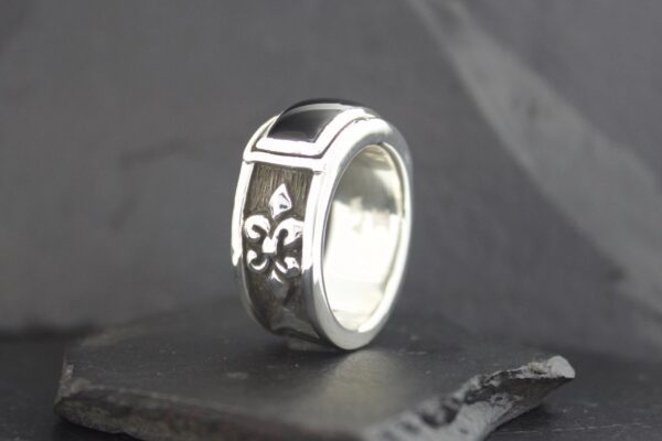 Silver ring with black fleur-de-lis design on a dark surface.