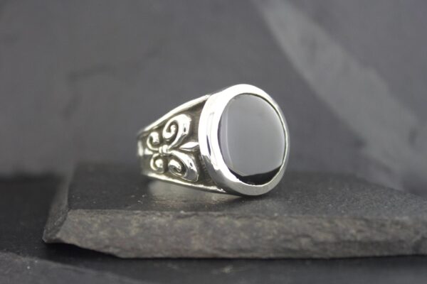 Silver ring with a black oval stone and intricate swirl designs.