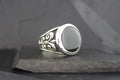 Silver ring with a black oval stone and intricate swirl designs.
