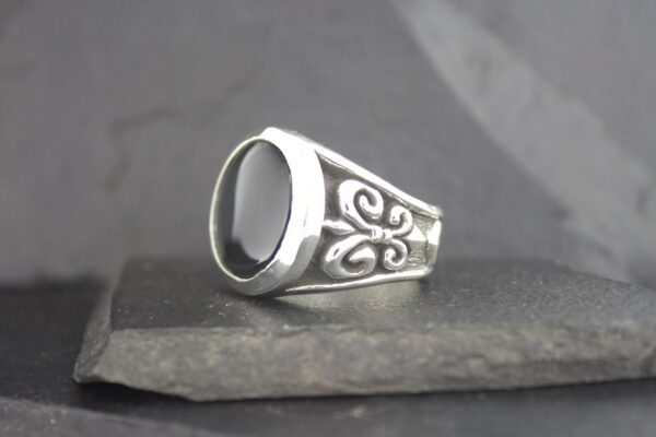Silver signet ring with ornate side engravings on a stone surface.