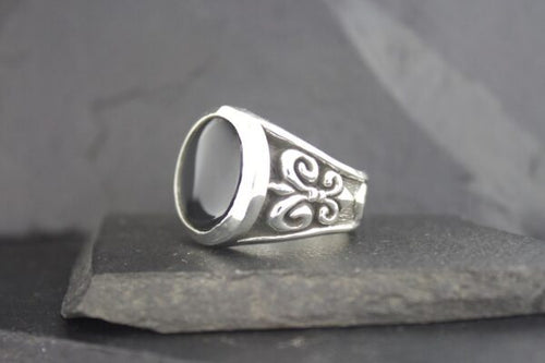 Silver signet ring with ornate side engravings on a stone surface.