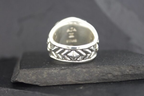 Silver ring with intricate geometric patterns on a dark surface.