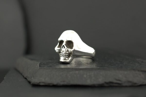 A silver ring featuring a detailed skull design on a dark surface.