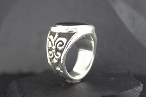 Silver ring with ornate floral design on black background.