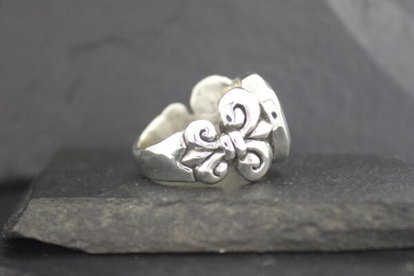 Silver ring with floral and swirl design on a dark stone surface.