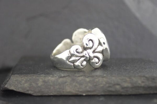 Silver ring with floral and swirl design on a dark stone surface.