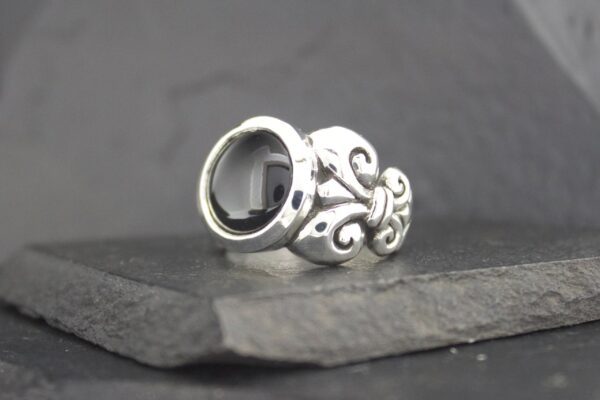 Ornate silver ring with an empty circular setting on a dark surface.