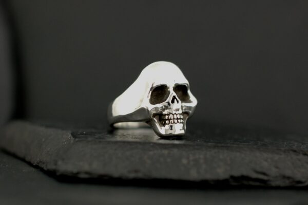 Silver skull-shaped ring on a dark surface.