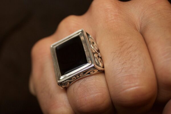 A hand wearing a silver ring with a large black rectangular stone.