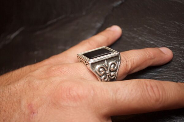 Ornate silver ring with a large black stone worn on a finger.