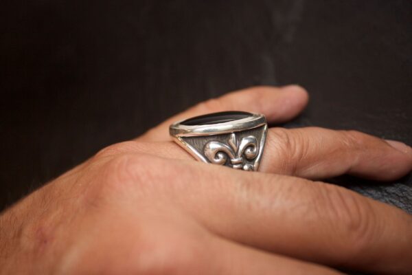 Silver ring with fleur-de-lis design on finger.