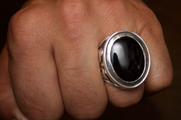 Close-up of a hand wearing a silver ring with a large black stone.