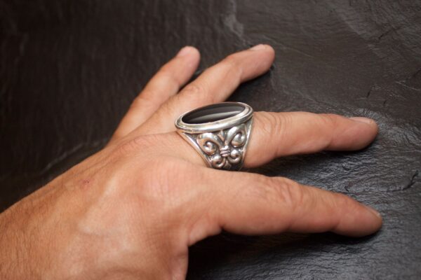 A hand wearing an ornate silver ring with floral designs.