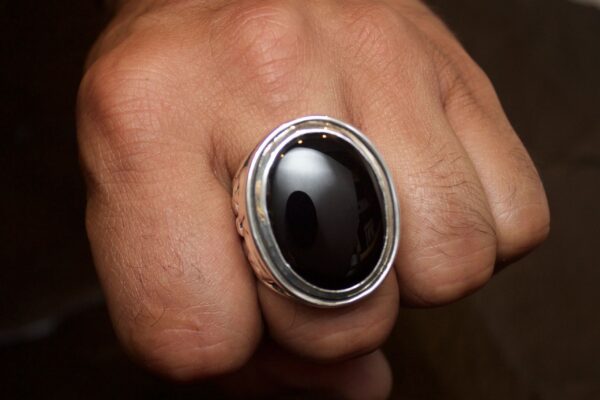 Close-up of a hand wearing a silver ring with a large black stone.