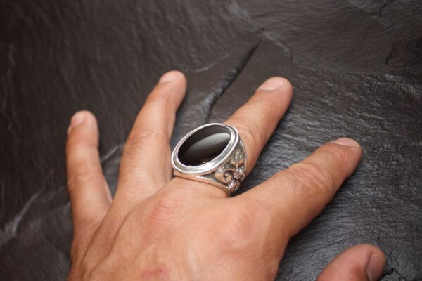 Hand with a silver ring featuring an intricate design on a dark surface.