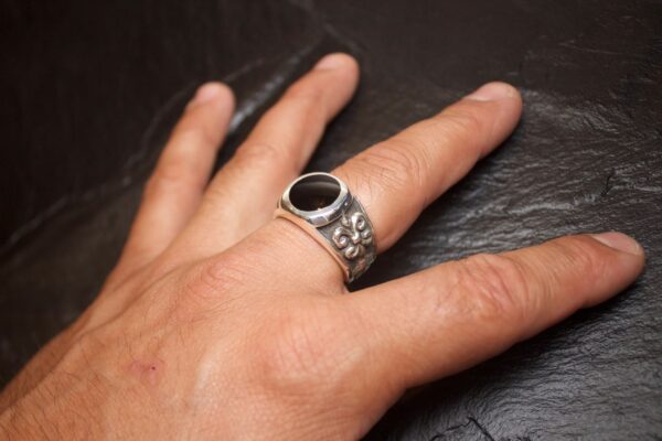 Hand wearing a silver ring with a black stone on a dark surface.