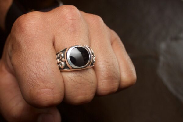 Close-up of a hand wearing a silver ring with a black stone.