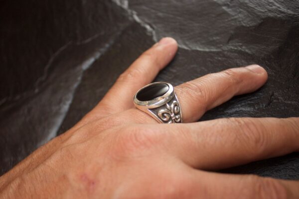 A hand wearing an ornate silver ring with a black stone.