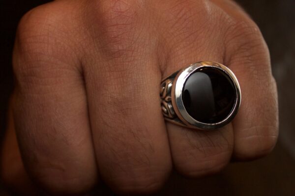 Close-up of a hand wearing a silver ring with a black stone.