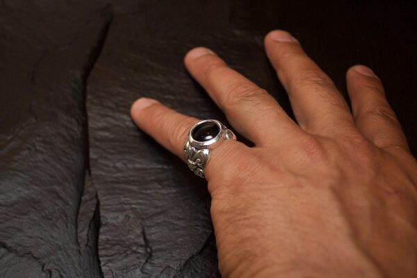 Hand wearing a silver ring with a black stone on a dark surface.