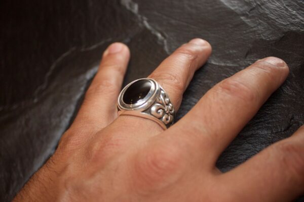 Hand wearing a silver ring with a black stone and intricate designs.