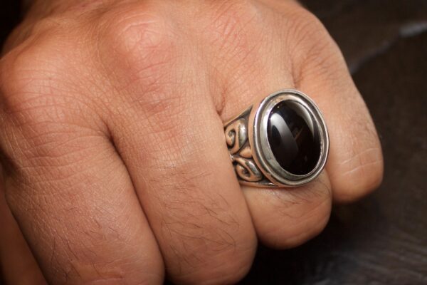 Close-up of a hand wearing a silver ring with a black stone.