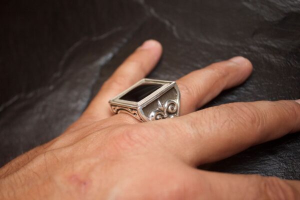 A close-up of a hand wearing a stylish silver ring with intricate designs.