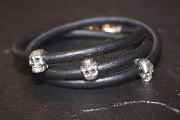Black leather bracelet with silver skull charms.