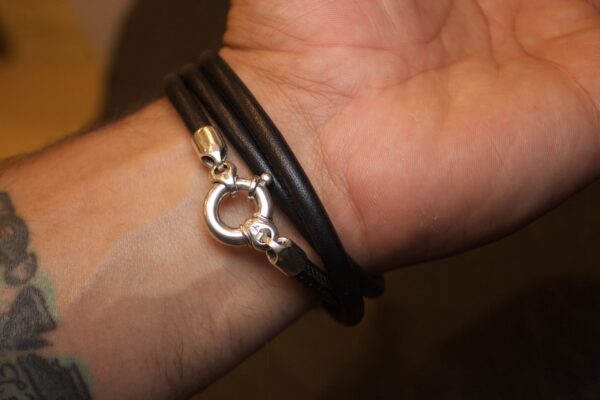 Close-up of a wrist wearing a black leather bracelet with a silver clasp.