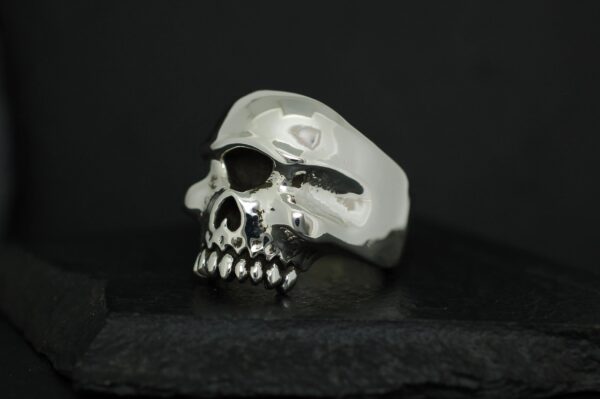 A silver skull-shaped ring with detailed teeth on a black background.