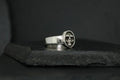 Silver ring with a unique circular emblem on a dark surface.