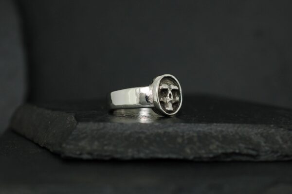 Silver ring with a unique circular emblem on a dark surface.
