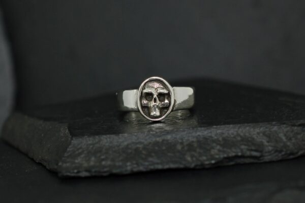 Silver ring featuring a detailed skull design on a dark background.