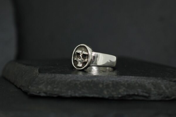 Silver ring with a compass design on a dark stone surface.