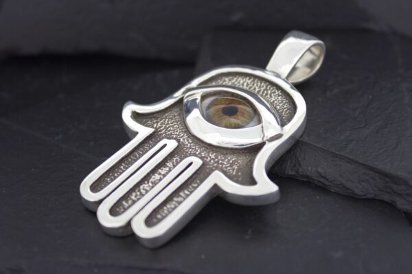 Silver Hamsa hand pendant with an eye design on a black background.