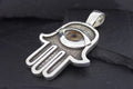 Silver Hamsa hand pendant with an eye design on a black background.