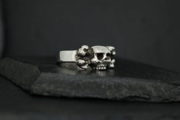 Silver ring with a skull design on a dark surface.
