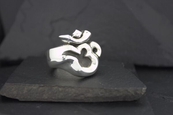 A silver ring featuring the Om symbol on a dark background.