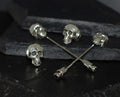 Silver skull-themed pins on a dark surface.