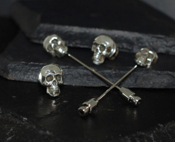 Silver skull-themed pins on a dark surface.