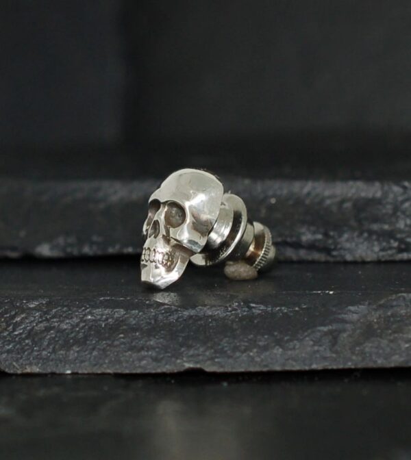Small metallic skull-shaped stud earring on a dark surface.