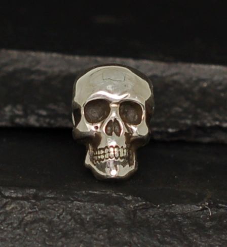 A metallic skull pin placed on a dark surface.
