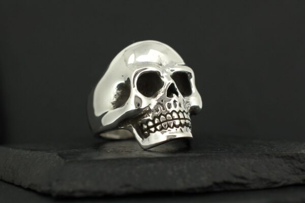 A shiny silver skull-shaped ring on a black surface.